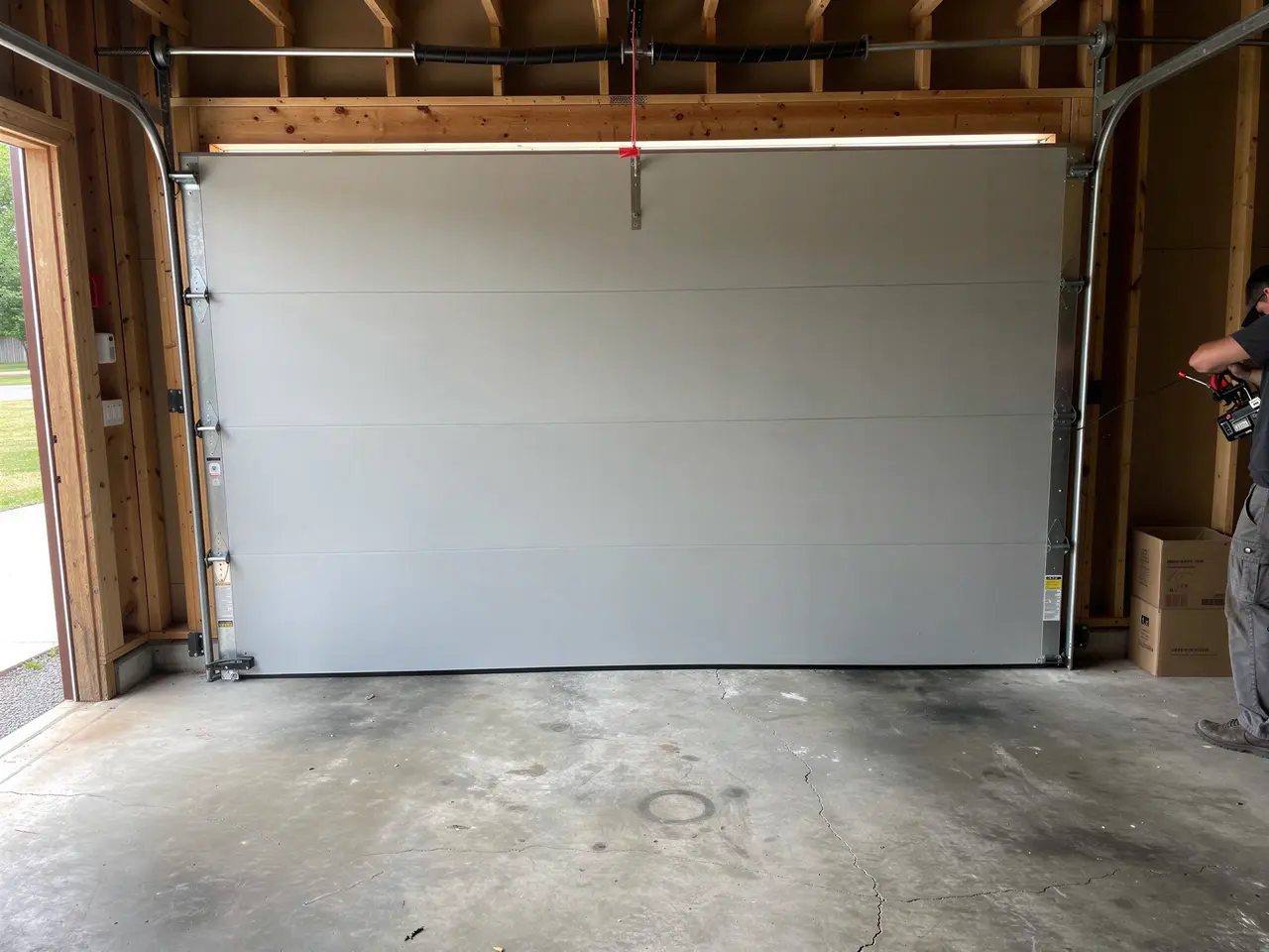 A technician works on a light gray garage door inside a garage.